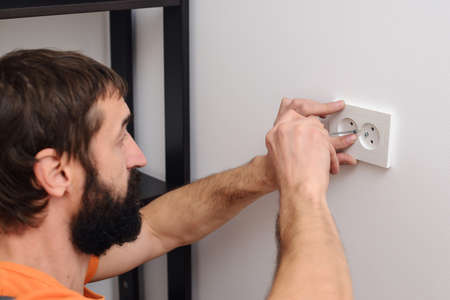 Worker installing socket in new house. Man installing light switch after home renovation. Electrician mounting electric sockets on the white wall. Electrician wiring a new build.の写真素材