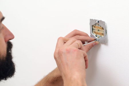 Electrician mounting electric sockets on the white wall. Electrician wiring a new build. Worker...
