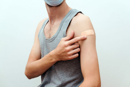 Man getting covid vaccinated. Person wearing face mask. Happy man showing his arm with bandage after...