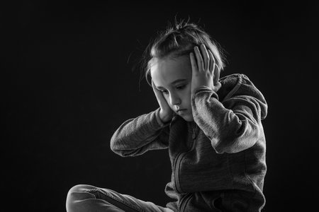 Young boy suffering from psychological diseases, anxiety. Unhappy sad boy over black background. Stress kid sitting alone in the dark.の写真素材