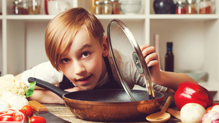 child cooking. Cute little chef holding frying pan at kitchen. Funny boy wearing apron. future profession. Chef trying a new recipe. Boy at cooking classes.の写真素材