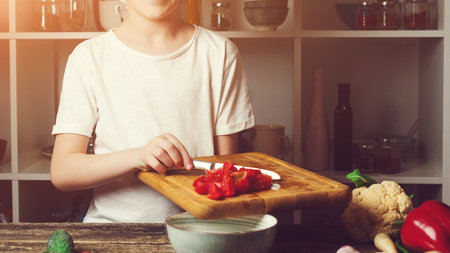 Little chef cutting fresh cherry tomatoes for salad. future profession. Boy at cooking classes. Cute child cooking salad for family dinner. Boy wearing chef's hat. Kid wants to be professional chef.の写真素材