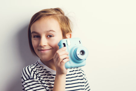 Cute boy holding photo camera. Stylish kid posing over gray background. Child with fun emotion and expression. fashion and technology.の写真素材