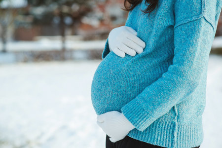 Pregnant woman in blue sweater touching big belly with hands. Warm clothes in cold weather. Pregnancy time. baby expectation. Pregnant woman's belly over winter background.の写真素材