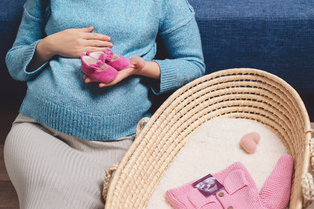 Happy mother enjoying pregnancy with wicker basket of cute tiny stuff newborn. Beautiful pregnant...