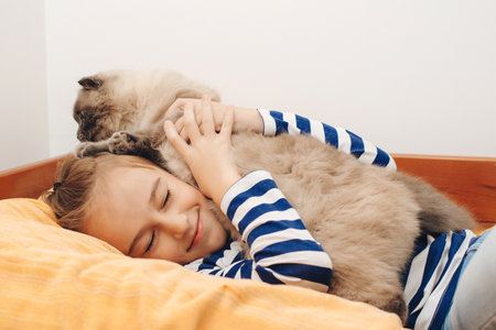 Cute boy plays with a cat at home. Happy kid hugging his cat. Boy relaxing on the bed with pet. Childhood, true friendship and home pet.の写真素材