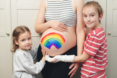 Cute boy with sister drawing rainbow on pregnant belly their mother. Baby birth expecting time and belly painting. Happy children and pregnant mom having fun together at home.の写真素材