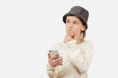 Smart kid holding a mobile phone. Technology, lifestyle and people concept. Cute boy using a smart phone over white background. Pensive young boy with a serious face thinking about a question.の写真素材