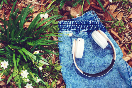 Wireless headphones on spring background, top view. Music, lifestyle and technology concept. White headphones on the denim jacket. Spring flowers and headphones.の写真素材