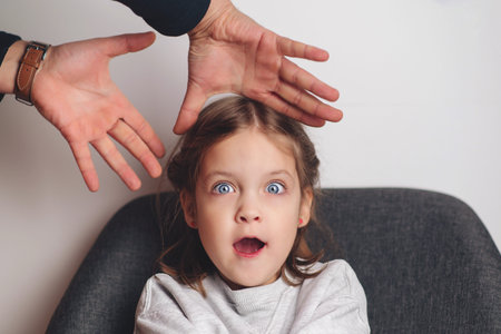 Sad offended child girl sitting at sofa at home. child abuse. Father yelling at his daughter. Violence, domestic problem in family.の写真素材