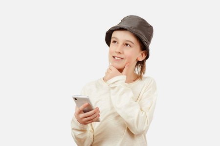 Pensive young boy with a serious face thinking about a question. Smart kid holding a mobile phone. Technology, lifestyle and people concept. Cute boy using a smart phone over white background.の写真素材