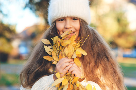 Happy child playing with autumn leaves on the nature walk. Little girl wearing warm knitted sweater. Autumn kids fashion, lifestyle.の写真素材