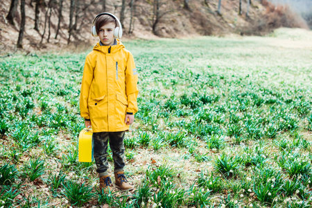 Cute boy walking at nature. Kid with headphones relaxing in the spring park. Stylish kid with headphones in the park.の写真素材