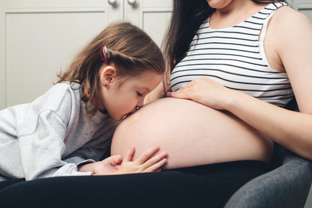 Pregnant woman with her little daughter at home. Cute little girl kisses her mother's tummy. Happy pregnant woman, her child, expectation.の写真素材
