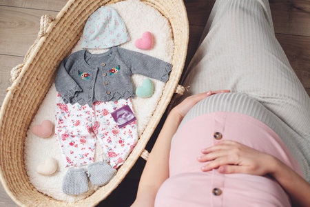 Happy mother enjoying pregnancy. Wicker basket of cute tiny stuff newborn. Beautiful pregnant woman at home. Pregnant woman preparing for baby birth her daughter.の写真素材