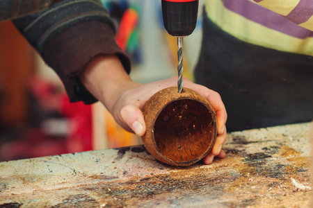 Creative student doing his project in workshop. Boy in the workshop makes crafts with coconut. School, development and learning concept. Young carpenter working in craft workshop.の写真素材