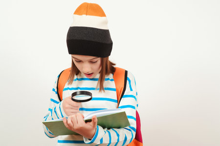Boy looking through magnifying glass to the book. Schoolboy holding the magnifying glass. Children's interest. Portrait of student boy with magnifier. School, learning and development concept.の写真素材