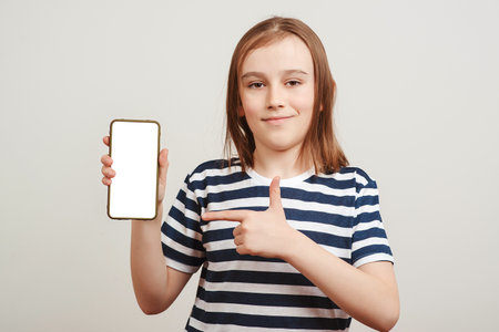 Happy boy showing to camera and pointing at empty free space. Background with free space, mockup. Smiling student in casual. Young guy holding smartphone.の写真素材