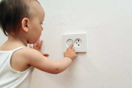 Baby touching the power socket. Baby and child safety concept. Curious little boy playing with electric plug. Child put finger in socket.の写真素材