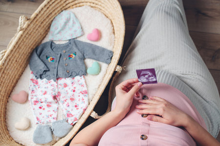 Happy mother enjoying pregnancy. Wicker basket of cute tiny stuff newborn. Beautiful pregnant woman at home. Pregnant woman preparing for baby birth her daughter.の写真素材