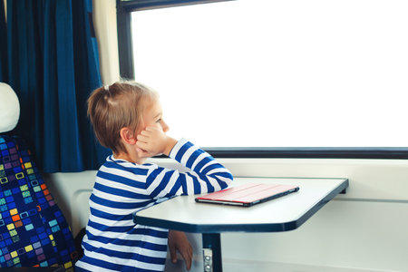 Little boy is traveling on the train. Kid travels on a train. Cute child looking out the train window. Childhood, family vacation, lifestyle.の写真素材
