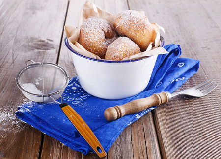 Freshly baked cinnamon sugared doughnuts in  a metal rustic bowl on a  blue napkin with sieve and fork on wooden background close up. Rustic still lifeの写真素材