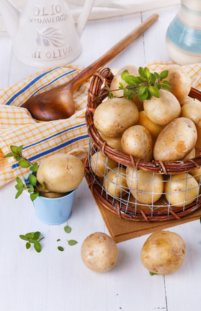 Fresh organic potatoes with thyme in a vintage rustic basket on white wooden backgroundの写真素材