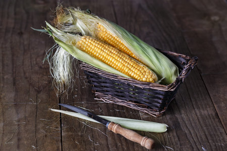 Sweet corns in a woven basket on dark rustic wooden background. Selective focus, shallow dof