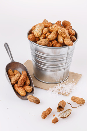 Roasted peanuts in shells in a metal bucket over white backgroundの写真素材