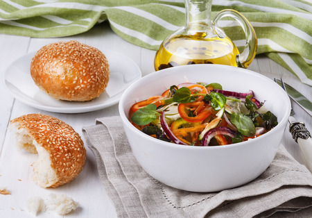 Colorful vegetable salad and dinner rolls over white wooden backgroundの写真素材