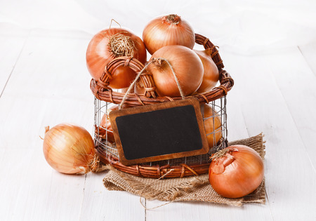 Group of brown onions in a metal basket over white wooden の写真素材