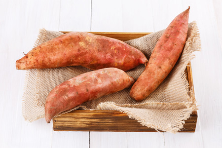 Sweet potatoes in a wooden box over white wooden backgroundの写真素材