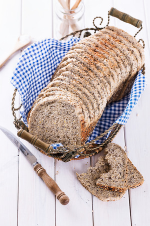 Sliced multigrain sandwich bread loaf in a metal basket on white wooden tableの写真素材