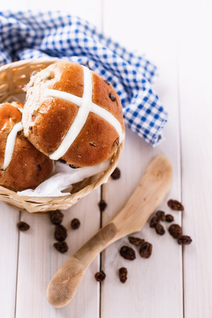 Tasty Easter cross-buns served on a woven basket, eco wooden knife and raisins on white wooden background. Selective focus, shallow depth of fieldの写真素材