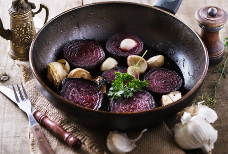 Roasted beetroot and garlic on a metal pan over rustic wooden background closeup. Selective focusの写真素材