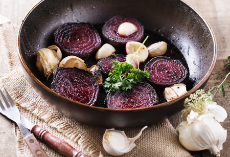 Roasted beetroot and garlic on a metal pan over rustic wooden background closeup. Selective focusの写真素材