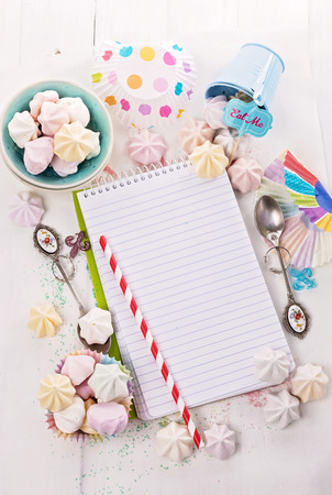 Cooking concept. Recipe book, meringue drops and party decorations over white wooden background with Copy spaceの写真素材
