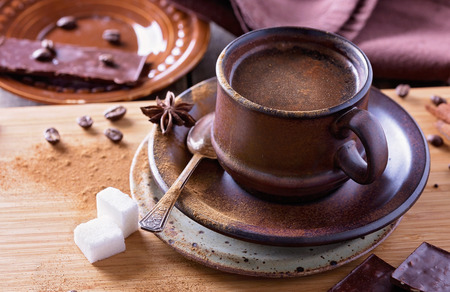 Spiced coffee in a textured ceramic cup with cinnamon powder, anis stars, sugar and pieces of chocolate over wooden table closeup. Selective focus, shallow depth of fieldの写真素材