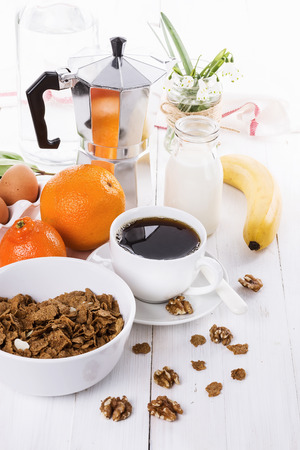 Breakfast with coffee, muesli, fruits and walnuts over white wooden backgroundの写真素材