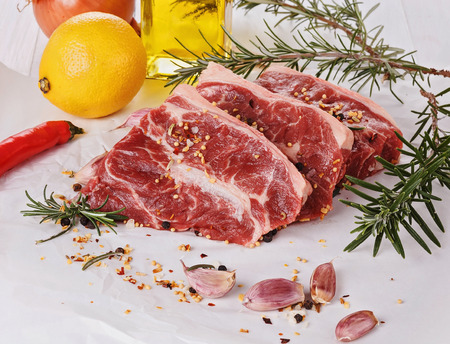 Tree pieces of red meat, vegetables and herbs over white backgroundの写真素材