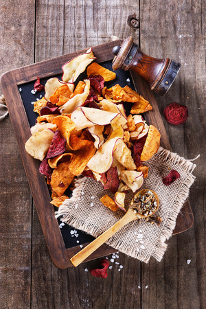 Healthy vegetable beetroot, sweet potato and white sweet potato chips on a black board with spoon of seasoning and salt shaker over rustic background. Top viewの写真素材