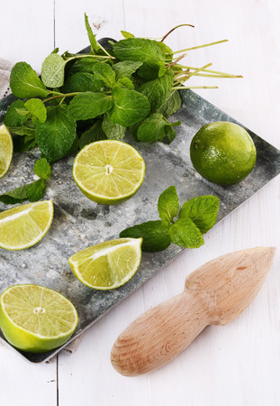 Limes halves and quarters and mint leaves in a vintage metal tray over rustic white wooden background. Selective focusの写真素材