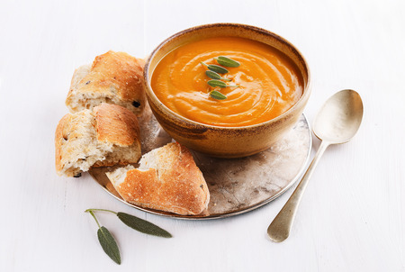 Bowl of creamy pumpkin soup with sage leaves and rustic bread on a silver tray on a wooden white background. Selective focusの写真素材