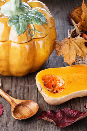 Autumn fall still life with butternut pumpkin, pumpkin shaped soup tureen and colourful leaves over dark rustic backgroundの写真素材