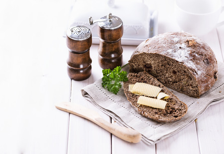 Freshly baked rye sourdough bread and bread slice with butter on white wooden background. Copy space, selective focus, shallow depth of fieldの写真素材