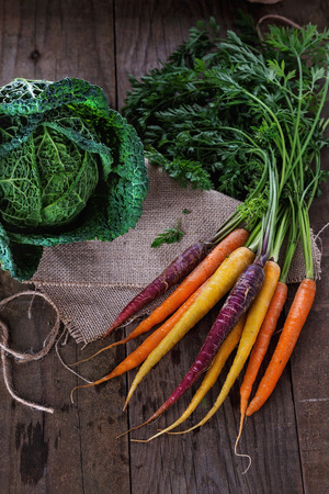 Single head of Savoy cabbage and bunch of colored carrots over rustic wooden backgroundの写真素材