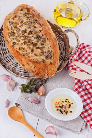 Freshly baked rustic sourdough bread with seeds and grains, garlic and infused oil over white wooden backgroundの写真素材