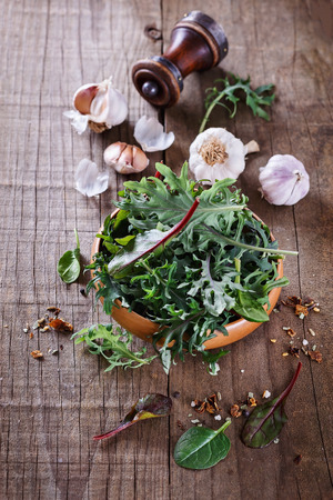 Leafy green mix of kale, spinach, baby beetroot leaves and garlic over rustic wooden backgroundの写真素材