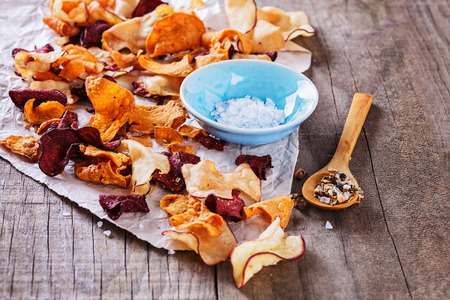 Healthy vegetable beetroot, sweet potato and white sweet potato chips with spoon of seasoning and salt over rustic background. Selective focus, front view of the image in not in focusの写真素材