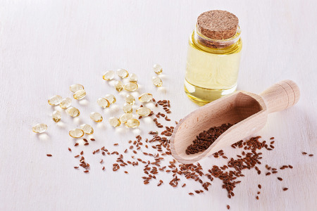 Linseed, flaxseed oil capsules and flaxseed oil over white wooden backgroundの写真素材